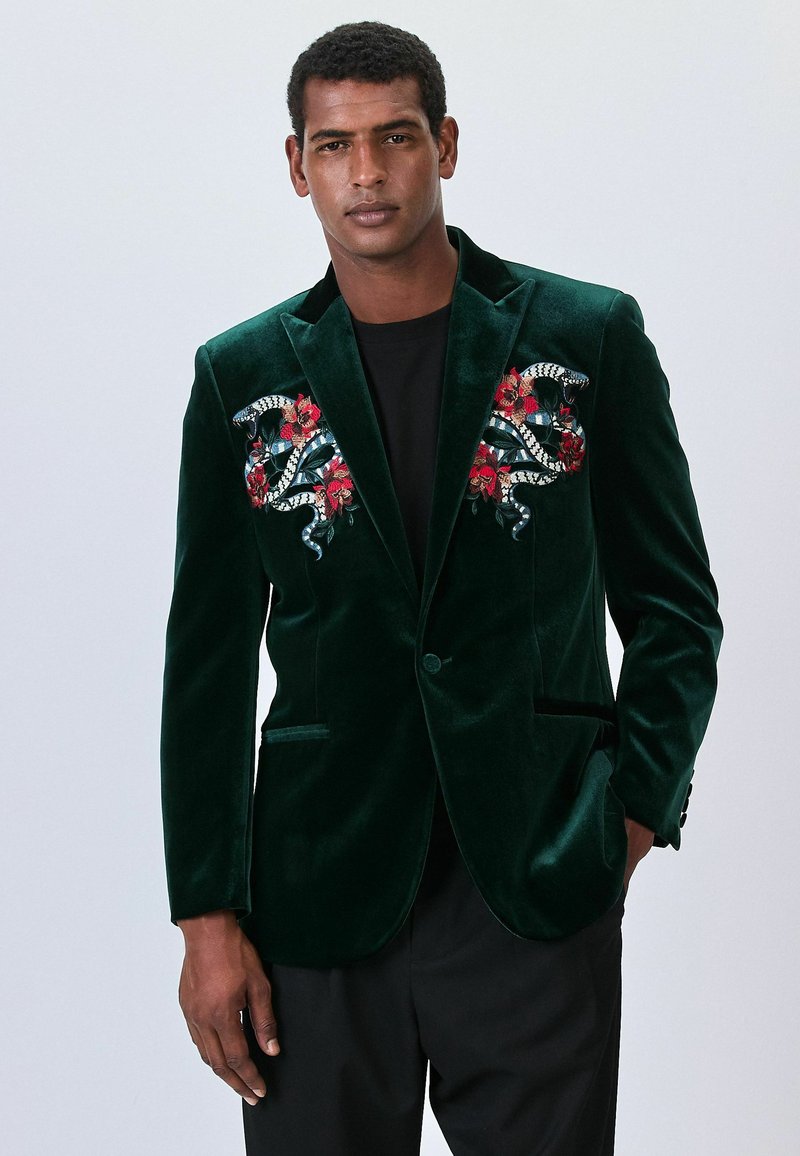 Green velvet blazer with embroidered snake and floral designs on the chest, notched lapels, and front pockets.