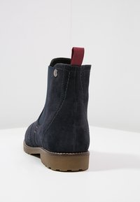 Bottine en daim bleu marine avec panneau latéral élastique, tirant maroon et semelle en caoutchouc marron. Présente des détails de couture et une silhouette épurée.