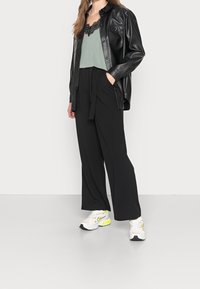 Sort faux læder skjortejakke, lysegrøn cami-top med blondekant, sorte brede bukser og hvide sneakers med neonlys.