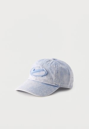 Casquette de baseball en jean bleu clair avec un patch ovale usé sur le devant et une visière incurvée, sur fond blanc uni.