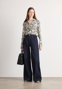Long-sleeve paisley-patterned blouse in cream and blue, paired with wide-leg dark denim jeans and a small black quilted handbag.