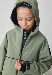 Olijfgroen gewatteerde jas met een volledige rits met branding, elastische manchetten en een gevoerde binnenkant voor extra warmte.