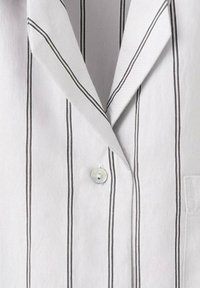 Chemise blanche à rayures noires verticales, avec un col pointu et un seul bouton fermé au centre devant.