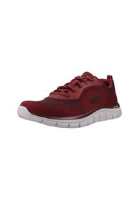 Zapatilla deportiva roja con una parte superior de malla transpirable, suela blanca flexible y acentos texturizados. Presenta cordones y una marca en el lateral.