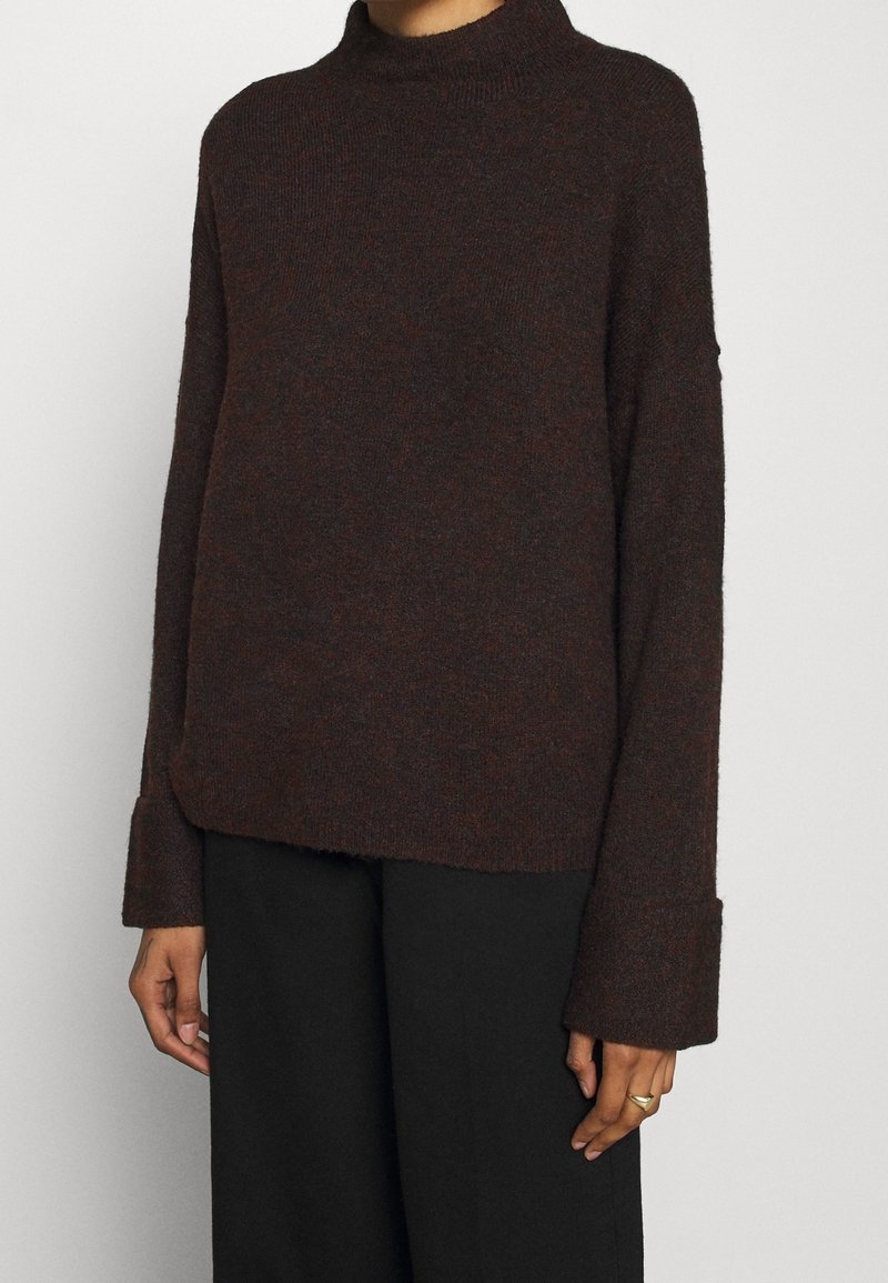 Ruskea turtleneck-paita, joka on valmistettu teksturoidusta neulekankaasta. Paidassa on pitkät hihat leveillä hihoilla ja rento istuvuus.