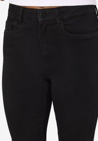 Jeans de ganga pretos com uma silhueta ajustada, apresentando fecho de botão, cinco bolsos e detalhes sutis de costura. Textura suave.