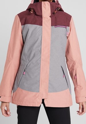 Vrouw draagt een colorblock-jas met stoffig roze mouwen, een grijze voorkant, bordeauxrode schouders, zakken met ritssluiting en een capuchon met trekkoorden.