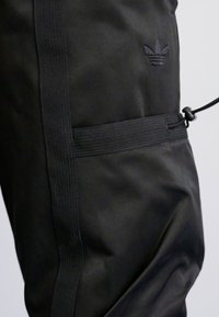 Calças atléticas pretas feitas de um tecido suave e leve; apresentam uma cintura elástica, cordão e logótipo em relevo de um lado.