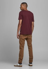 Burgunderfarbendes T-Shirt mit kurzen Ärmeln und Rundhalsausschnitt, kombiniert mit beigen Chinos und weißen Sneakers mit blauen und roten Akzenten.