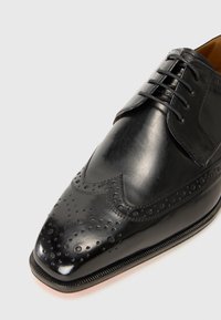 Svarte skinndressko med broguedesign og perforeringer, spiss tå og en glatt overflate. Inkluderer snøring og slank såle.