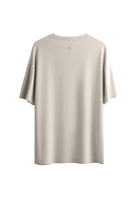T-shirt oversize beige chiaro realizzato in tessuto morbido. Presenta maniche corte, un colletto rotondo e un piccolo emblema a forma di forbice vicino al colletto posteriore.
