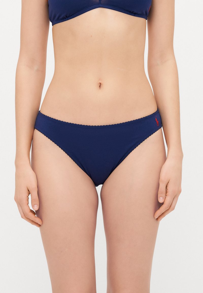 Navy blue cotton bikini briefs with a scalloped waistband, featuring a small red logo on the side. Smooth texture, simple design.