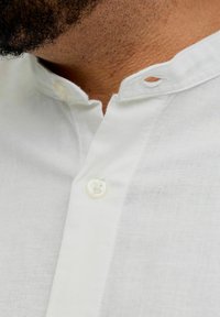 Gros plan sur le cou d'un homme et une chemise blanche à col avec un bouton fermé et une boutonnière sur le col.