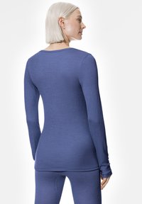 Femme aux cheveux blonds courts portant un haut bleu en côtes ajusté à manches longues et un bas assorti, vue de l'arrière et de côté.