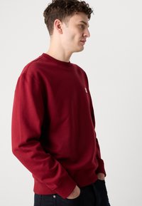 Felpa bordeaux con colletto rotondo, polsini e vita a coste. Presenta un piccolo logo sul petto e un tessuto morbido in misto cotone.