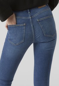Blå denimjeans med en åtsittande design, bakfickor och midjehöjd mitt emellan. Synligt sömnadsdetaljer och minimal blekning.