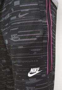 Svarta träningsbyxor med en texturerad grafisk design i grått, med rosa sidodetaljer och en vit Nike-logotyp nere till vänster.