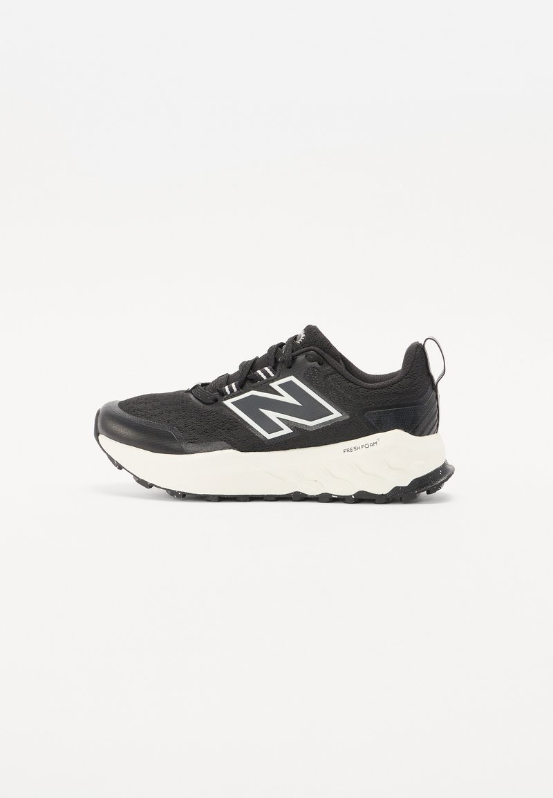Baskets de sport noires avec une tige en tissu texturé, une semelle intermédiaire blanche contrastante et un logo gris proéminent sur le côté. Semelle en caoutchouc avec traction.
