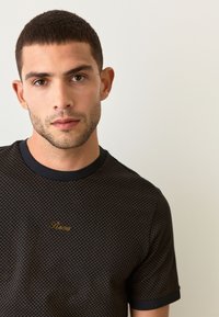 Black short-sleeve t-shirt with a textured pattern, featuring a round neckline and small gold "Roma" embroidery on the chest.