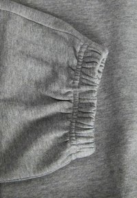 Grå sweatshirtens tyg med rynkade manschettdetaljer och en slät textur. Har en enhetlig nyans utan distinkta mönster eller accenter.