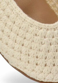 Tejido de ganchillo color crema con un patrón texturizado, que cubre una forma redondeada; plantilla interior beige y un acabado suave. Sin herrajes visibles.