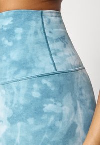 Magas derékú, világoskék, batikolt leggings puha anyagból, sima, texturált felülettel és látható varrási részletekkel a varratok mentén.