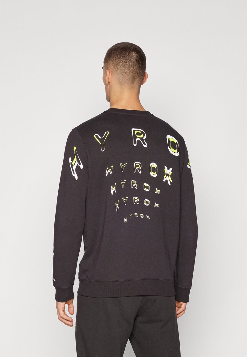 Svart sweatshirt laget av bomull med lange ermer, med hevet, flerfargede "HYROX"-grafikker på ryggen og ermene.