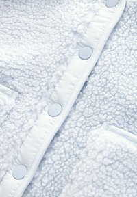 Lichtblauwe fleece stof met een gestructureerd, pluizig oppervlak, voorzien van gladde blauwe drukknoopjes en een zakdetail.
