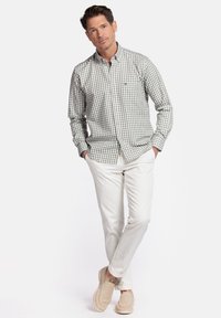 Groen en wit geruit overhemd met lange mouwen, gecombineerd met witte broek en beige instap schoenen. Eenvoudig, klassiek ontwerp.