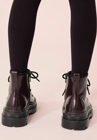 Bottines à plateforme noires en cuir bourgogne brillant, avec un design à lacets et des zips à l'arrière. Semelles en caoutchouc plates.
