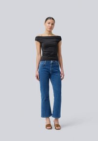 Black off-shoulder top, fitted design. Blue denim jeans, straight leg, medium wash. Brown slide sandals. Neutral background.