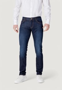 Vaqueros de denim azul oscuro con un corte recto, que cuentan con costuras contrastantes, bolsillos frontales y un cierre de botón, combinados con zapatillas blancas.