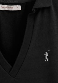 Svart pikétröja med V-halskrage, tillverkad av texturerat material. Har en liten vit broderad golfspelare-logotyp på vänster bröst.