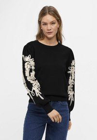 Pull noir avec des manches bouffantes ornées de délicates broderies florales beiges. Le design comprend des poignets côtelés et un col rond classique.