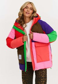 Farebná prešívaná bunda pozostávajúca z častí červenej, ružovej, zelenej, fialovej a hnedej farby, s prednou vreckom a kapucňou. Mäkká tkanina a voľný strih.
