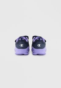 Baskets de sport violettes et bleu marine avec une tige texturée, une sangle ajustable et des semelles épaisses et rembourrées. Logo visible sur le talon.