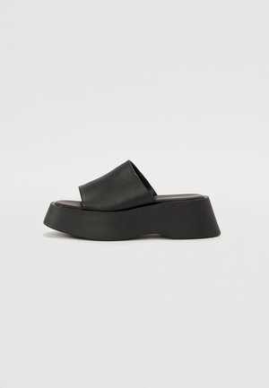 Black platform sandals featuring a wide strap and chunky sole. Made from smooth material with a matte finish and no visible hardware.