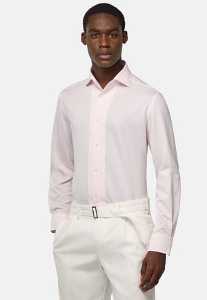 Camisa de manga larga de color rosa claro con botones en la parte delantera y collar, combinada con pantalones blancos a medida que presentan un cinturón negro y bolsillos laterales.