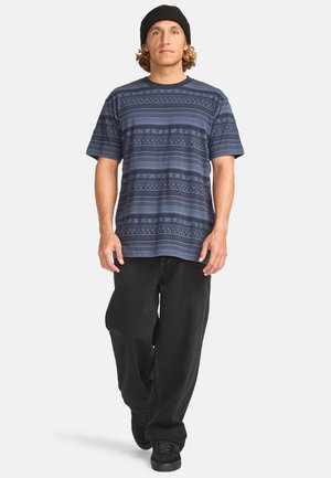 Navy short-sleeve shirt with geometric patterns and textured details, paired with black loose-fit pants and dark sneakers.