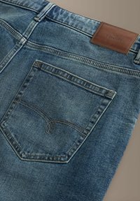 Spodnie dżinsowe z jasnoniebieskim wybarwieniem, z skórzaną metką na pasku oraz detalicznym przeszyciem na tylnej kieszeni.