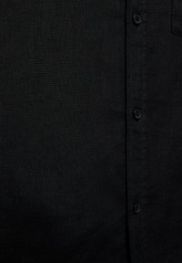 Tissu noir texturé avec une rangée verticale de trois boutons noirs et des coutures visibles sur le côté droit.