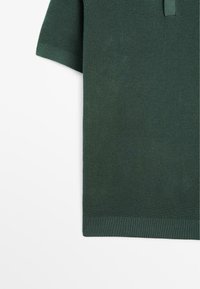 Polo shirt verde a trama con maniche corte, colletto e orlo a coste. Il tessuto presenta un motivo a maglia con una finitura traspirante.