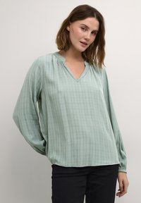 Blusa de manga larga y cuello en V en verde claro con un patrón de cuadros, hecha de tela ligera, con detalles fruncidos en el escote.
