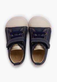 Námořnické modré boty s bílým gumovým špičkou, texturovaný kožený svršek a suchý zip. Má kontrastní švy a zlaté očka.