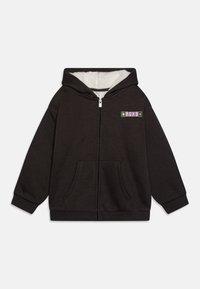 Čierna mikina na zips s mäkkou, nadýchanou bielou podšívkou. Má malú farebnú nášivku na ľavej strane hrudi a dve predné vrecká.