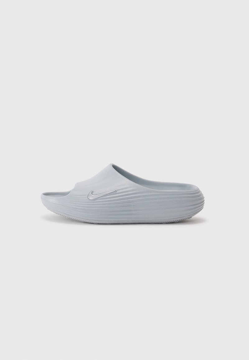 Sandale slide Nike gris clair avec des rainures texturées et un logo Nike en relief sur le côté, vue de profil.