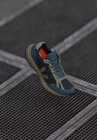 Pantof sportiv cu un superior din plasă neagră, cu accente albastre și khaki, talpă din cauciuc și brant portocaliu. Proiectat pentru confort și aderență.