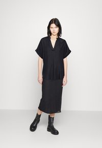 Top nero a maniche corte con scollo a V, abbinato a una lunga gonna nera. Entrambi presentano una texture liscia, completati da stivali neri alla caviglia.