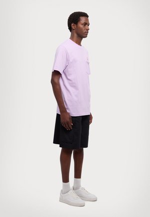 Lilas bomull t-skjorte med lomme og rund logo. Kombinert med sorte shorts og hvite sneakers. Enkel design med rund hals.