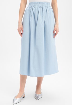 Femme portant une jupe midi bleu clair avec une taille élastique et des ballerines slingback argentées à bout pointu, debout sur un fond blanc.